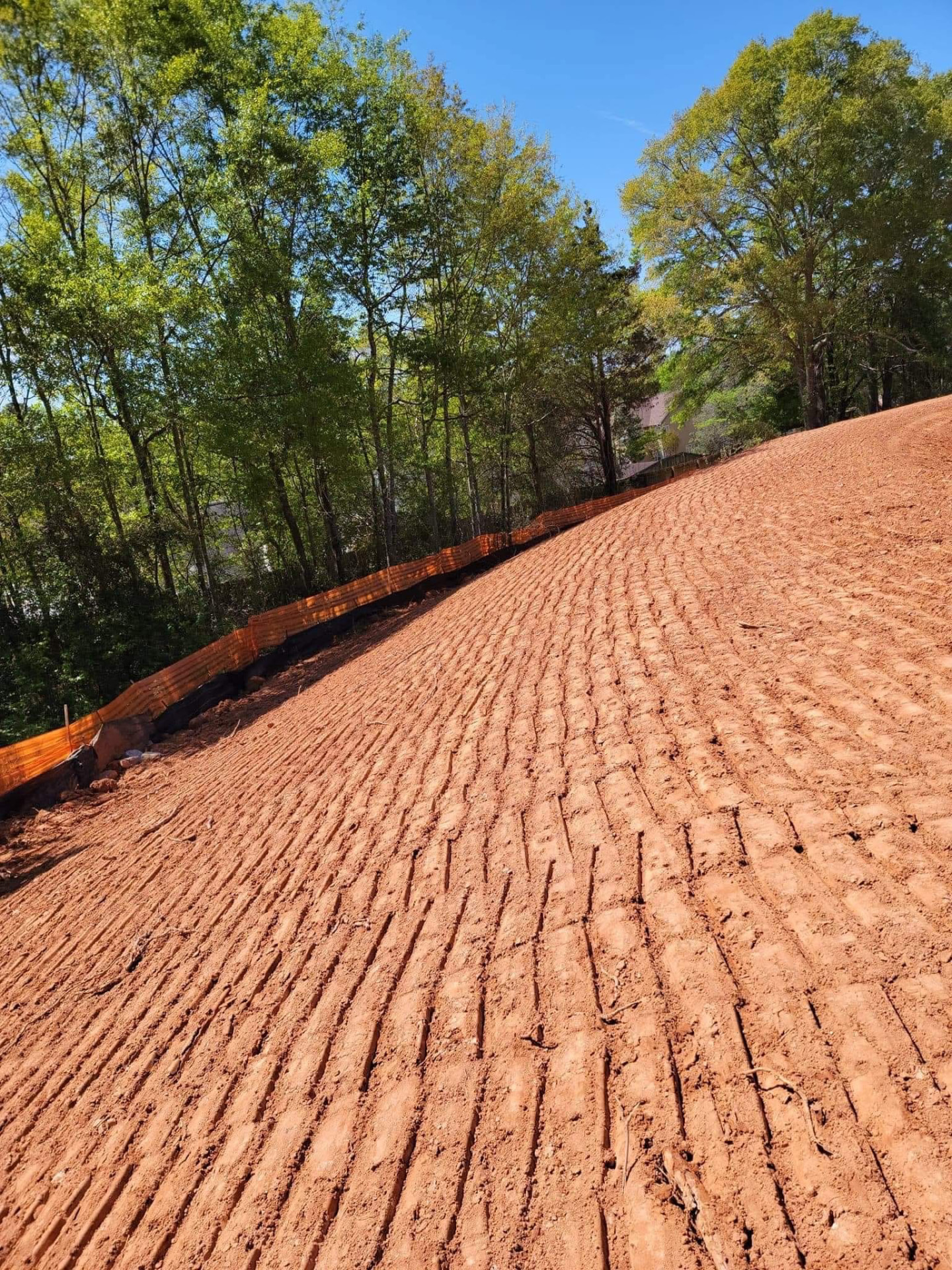Freshly finish-graded red clay slope with erosion control fencing