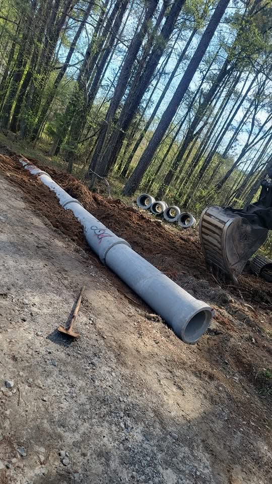 Concrete drainage pipe being installed beside an excavator